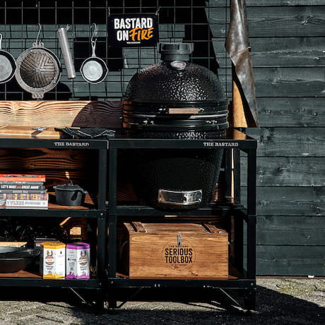 Outdoor-Küche mit Grill und Kochutensilien an einer schwarzen Wand