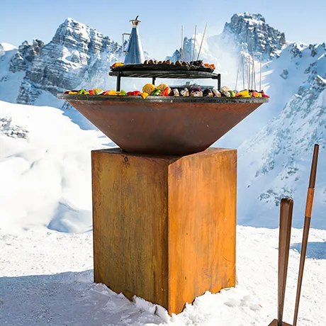 große-feuerschale-aus-cortenstahl-mit-buntem-grillgut-vor-einer-bergkulisse-im-schnee