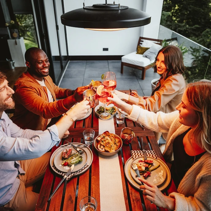 freunde-auf-einem-balkon-gemeinsam-an-einem-tisch-darüber-eine-heizstrahler