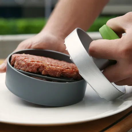 Hackfleisch in einer Burger presse und eine Person die es hält.
