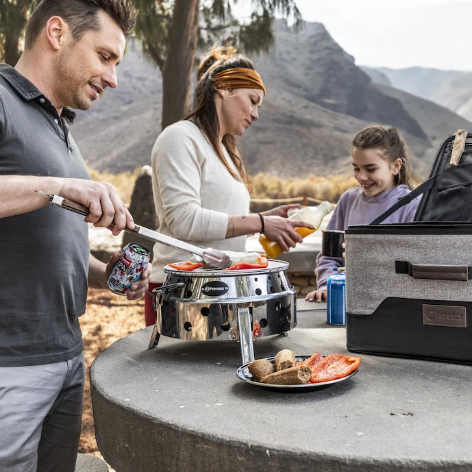 familie-steht-an-einem-petromax-atago-grill-auf-einer-wanderung-durch-die-berge