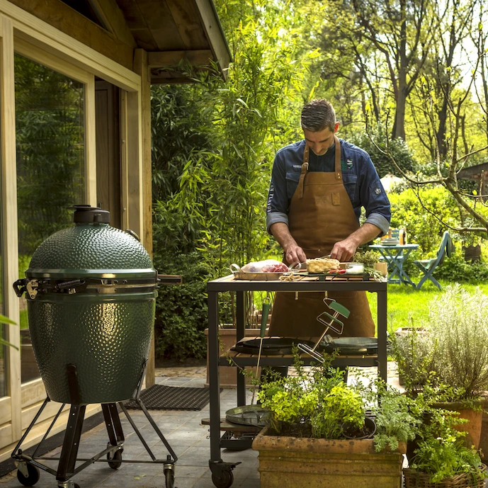 mann-bereitet-an-einem-arbeitstisch-speisen-vor,-daneben-steht-ein-big-green-egg-keramikgrill