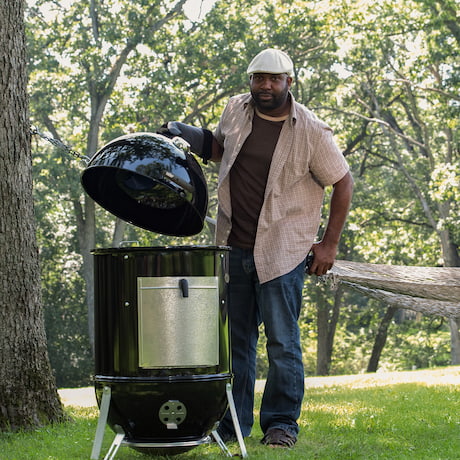 Mann öffnet den Deckel eines Smokey Mountain Cookers im Park