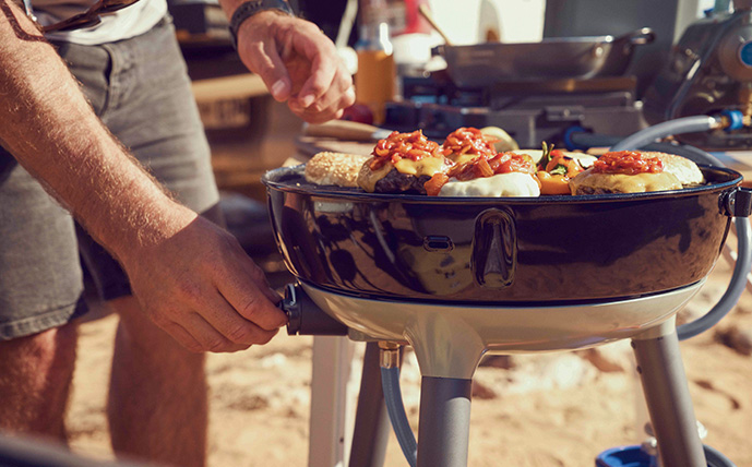 cadac-carri-chef-40-gasgrill-in-aktion-mit-grillgut-und-mann,-der-die-gaszufuhr-bedient