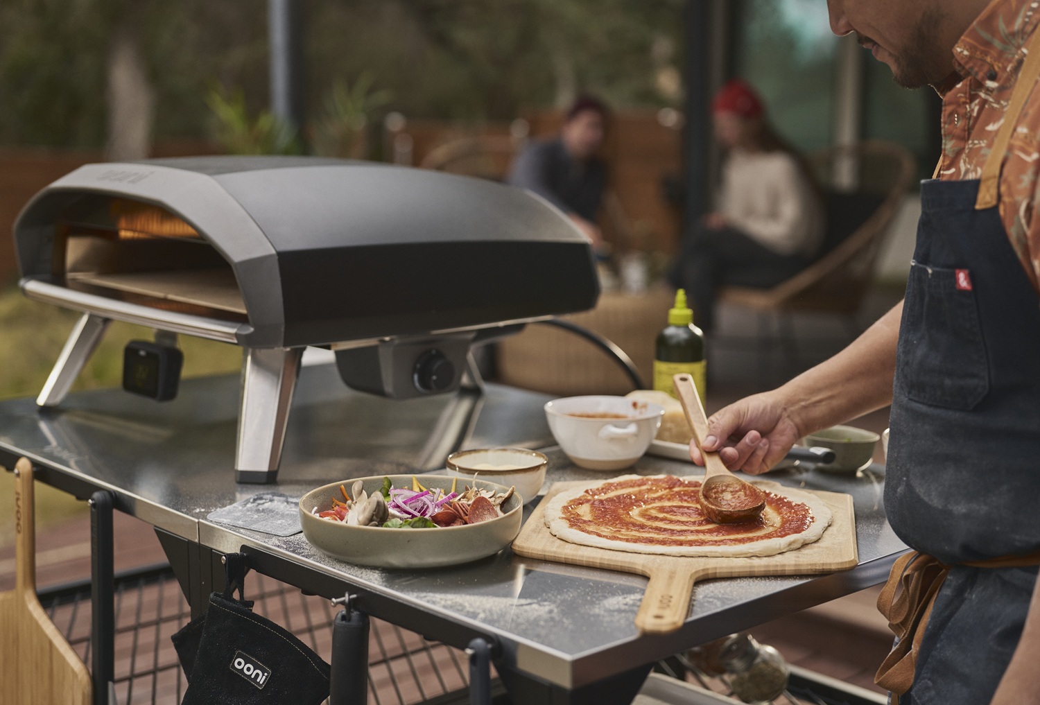 ooni-koda-2-pro-gas-pizzaofen-auf-einem-tisch,-daneben-bereitet-ein-mann-die-nächste-pizza-vor