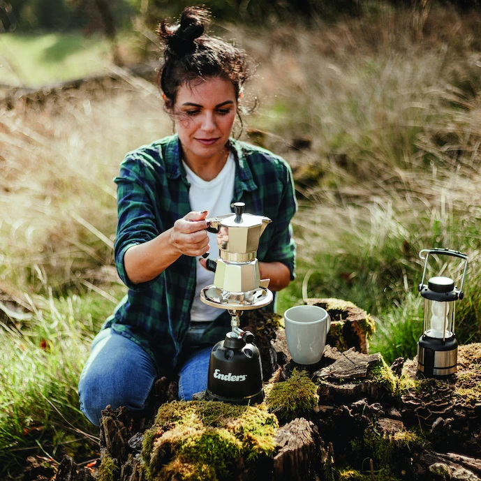 junge-frau-auf-einer-waldlichtung-mit-einem-enders-olymp-gas-campingkocher-darauf-eine-kaffeekanne