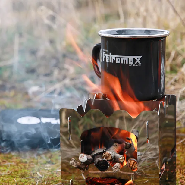 Kleiner Outdoor-Holzofen mit brennendem Feuer und Petromax-Tasse Kleiner Outdoor-Holzofen mit brennendem Feuer und Petromax-Tasse