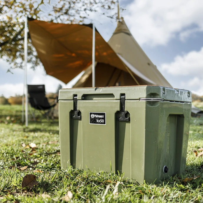 petromax-kühlbox-50-liter-in-oliv-auf-einem-campingplatz-vor-einem-zelt