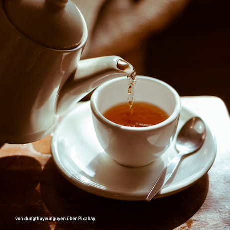 Weiße Teetasse und eine Kanne, die gerade Tee einschenkt
