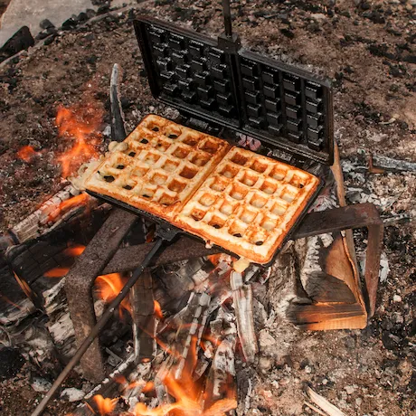 Ein Waffeleisen auf einem offenen Feuer mit Waffeln darin Ein Waffeleisen auf einem offenen Feuer mit Waffeln darin