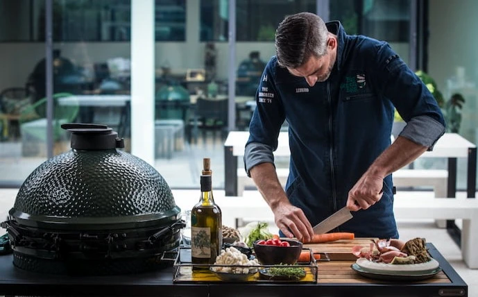 big-green-egg-keramikgrill-im-einsatz-daneben-ein-mann-bei-der-zubereitung-und-vorbereitung-des-grillguts