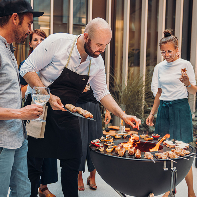 die-feuerschale-bowl-mit-plancha-und-grillgut-umrundet-von-gästen