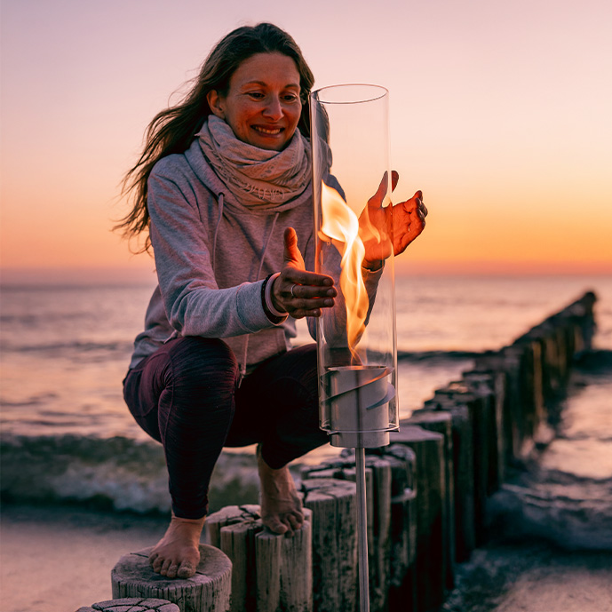 frau-bei-sonnenuntergang-am-meer-mit-einer-fackel-aus-glas-und-edelstahl,-die-brennt