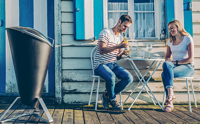 großer-geschlossener-holzkohlegrill-daneben-zwei-menschen-an-einem-tisch