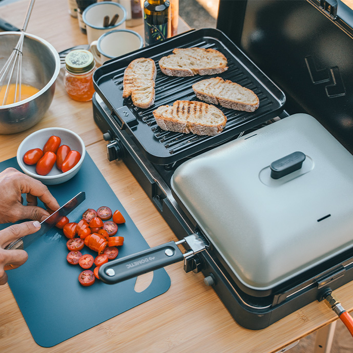 cadac-campingkocher-mit-zwei-flammen,-gasbetrieben-darauf-pfanne-mit-deckel-und-blech-mit-geröstetem-brot