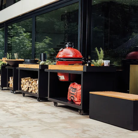 Ein Outdoor-Kochbereich mit einem großen roten Keramikgrill und verschiedenen modernen Holzmöbeln, in einem geräumigen Patio.